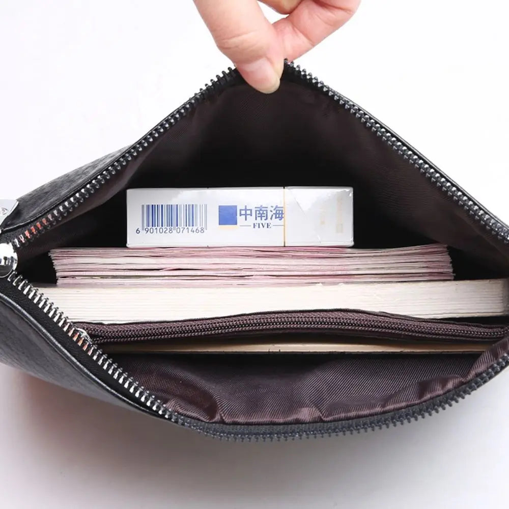 A hand is opening a dark brown PU leather clutch bag to reveal stacked papers inside.