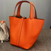 An orange classic genuine leather bucket bag with a flap closure is displayed on a gray surface.