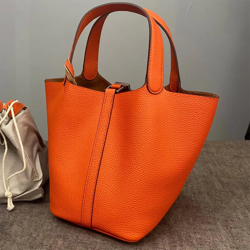 An orange classic genuine leather bucket bag with a flap closure is displayed on a gray surface.