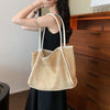 A woman holds a light beige straw woven tote bag with white trim against a wooden cabinet.