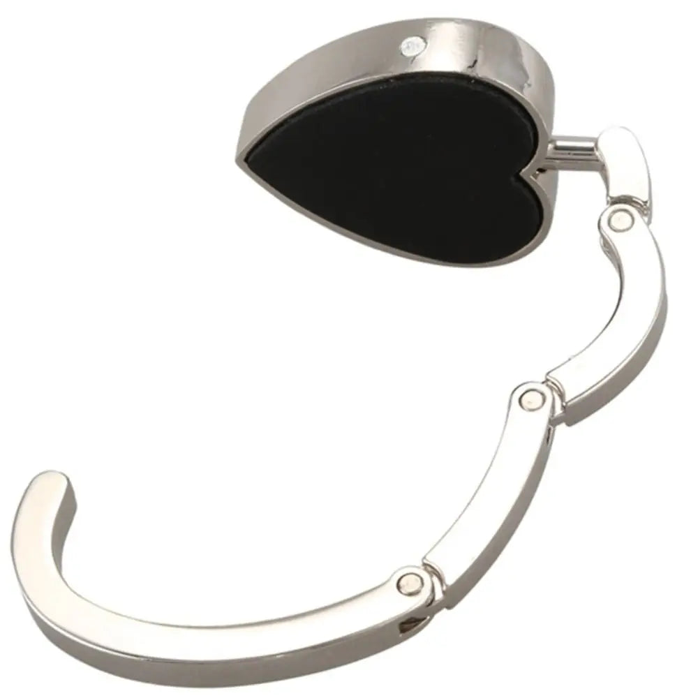 A silver heart-shaped metal foldable bag hook with a black heart design.