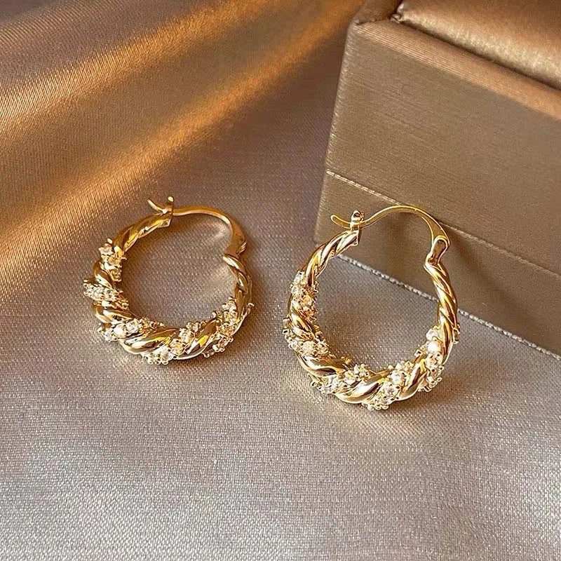 Eine goldene U-förmige geometrische Creolenohrringe mit strukturiertem geflochtenem Design auf einer neutralen Oberfläche.