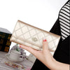 A hand holds an elegant gold diamond quilted long wallet with a crown buckle against a black and white striped background.