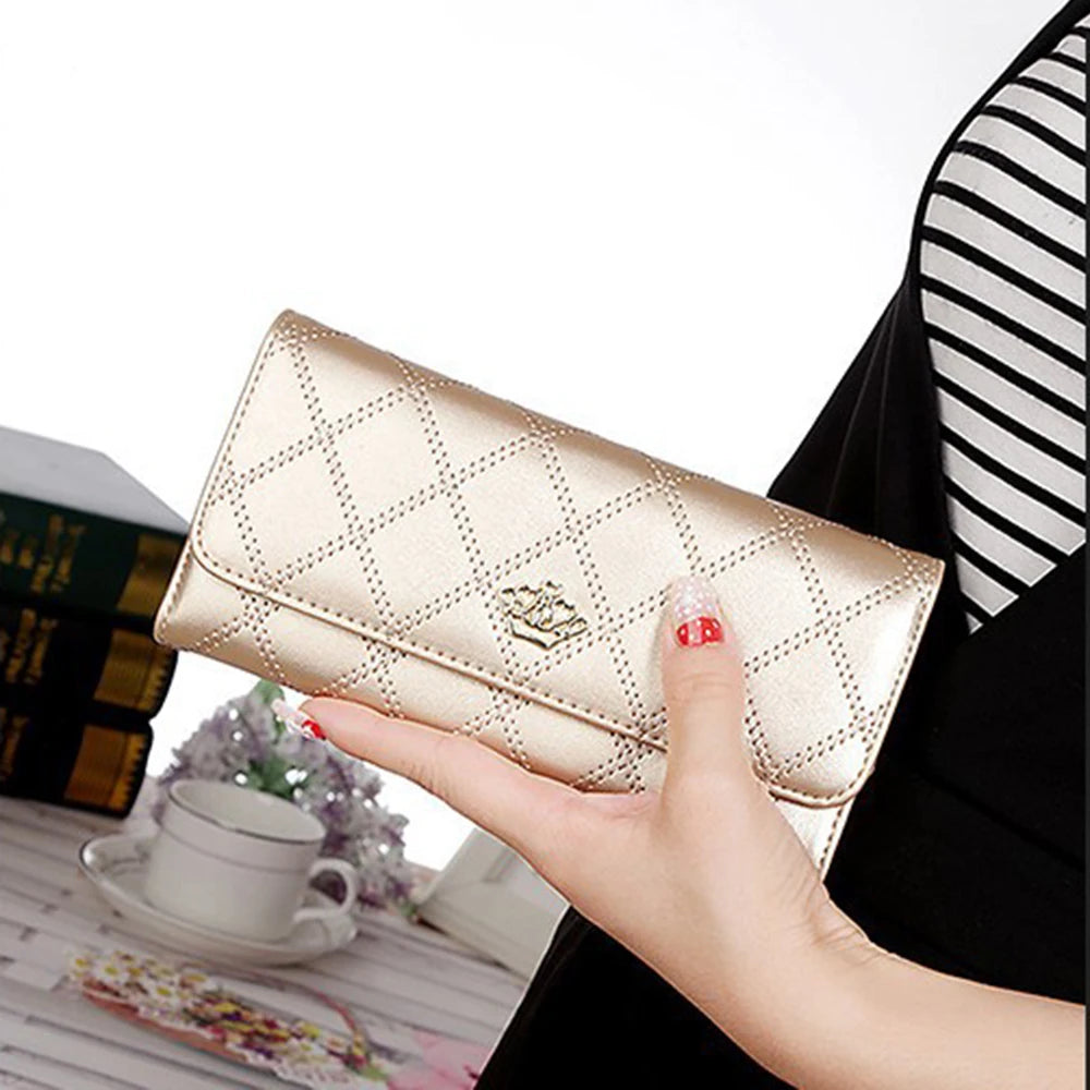 A hand holds an elegant gold diamond quilted long wallet with a crown buckle against a black and white striped background.