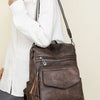 A woman holds a brown retro PU leather travel backpack with tassel detail against a light background.
