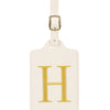 Étiquette de bagage en cuir crème rectangulaire avec un H brodé en or et un clip métallique argenté.
