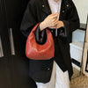 A person holds a reddish-brown woven embossed hobo shoulder bag with a top handle against a black jacket and white shirt.