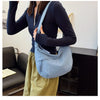 A woman wearing a dark blue top and light green skirt carries a blue canvas crossbody bag.