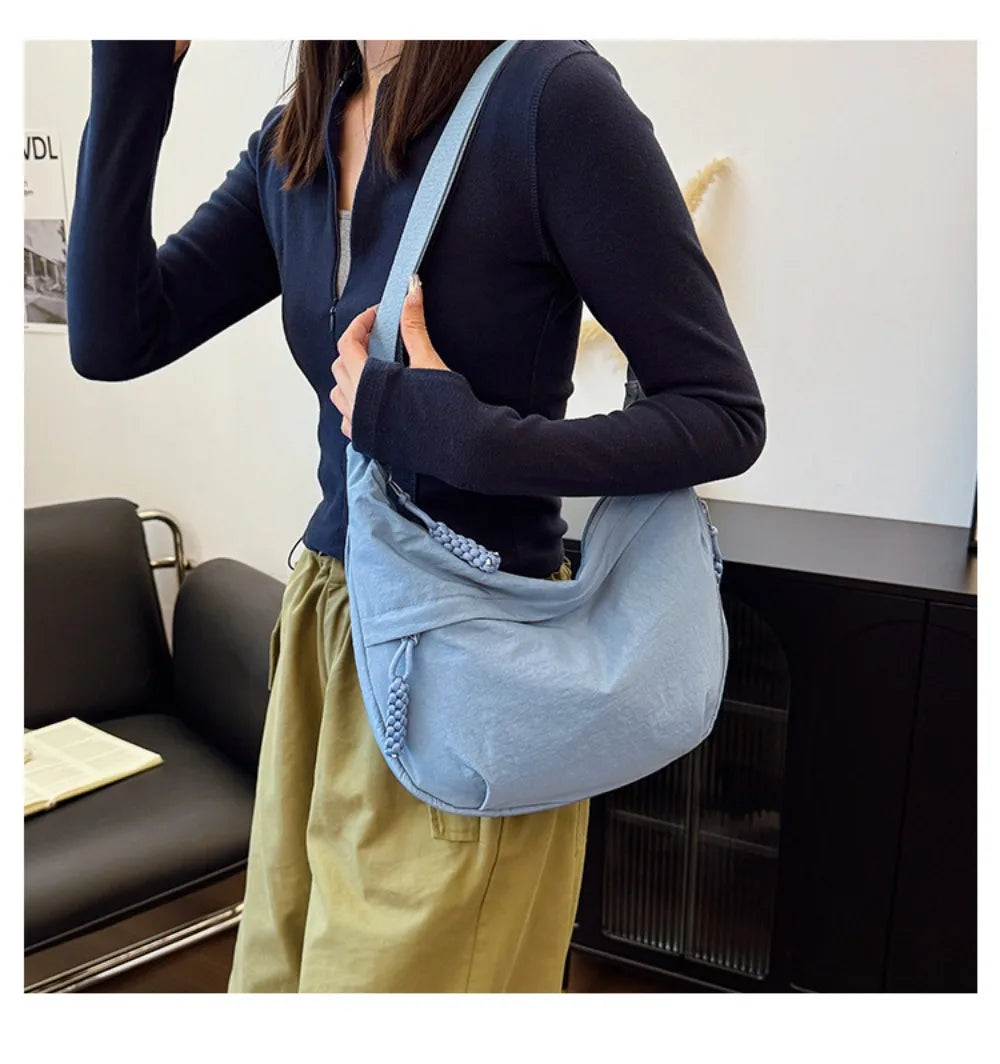 A woman wearing a dark blue top and light green skirt carries a blue canvas crossbody bag.