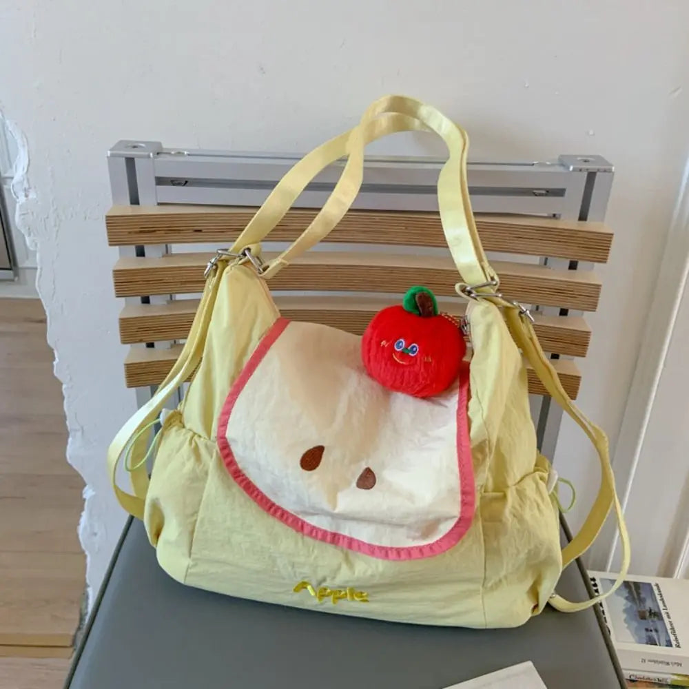 A yellow nylon messenger backpack shaped like a face with a red apple detail.