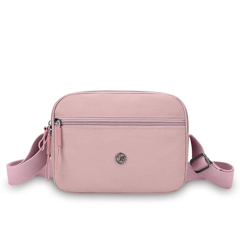 A light pink nylon crossbody bag with an adjustable strap shown from the front.