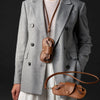 A woman wearing a gray blazer holds a brown PU leather eyewear storage case and glasses bag.