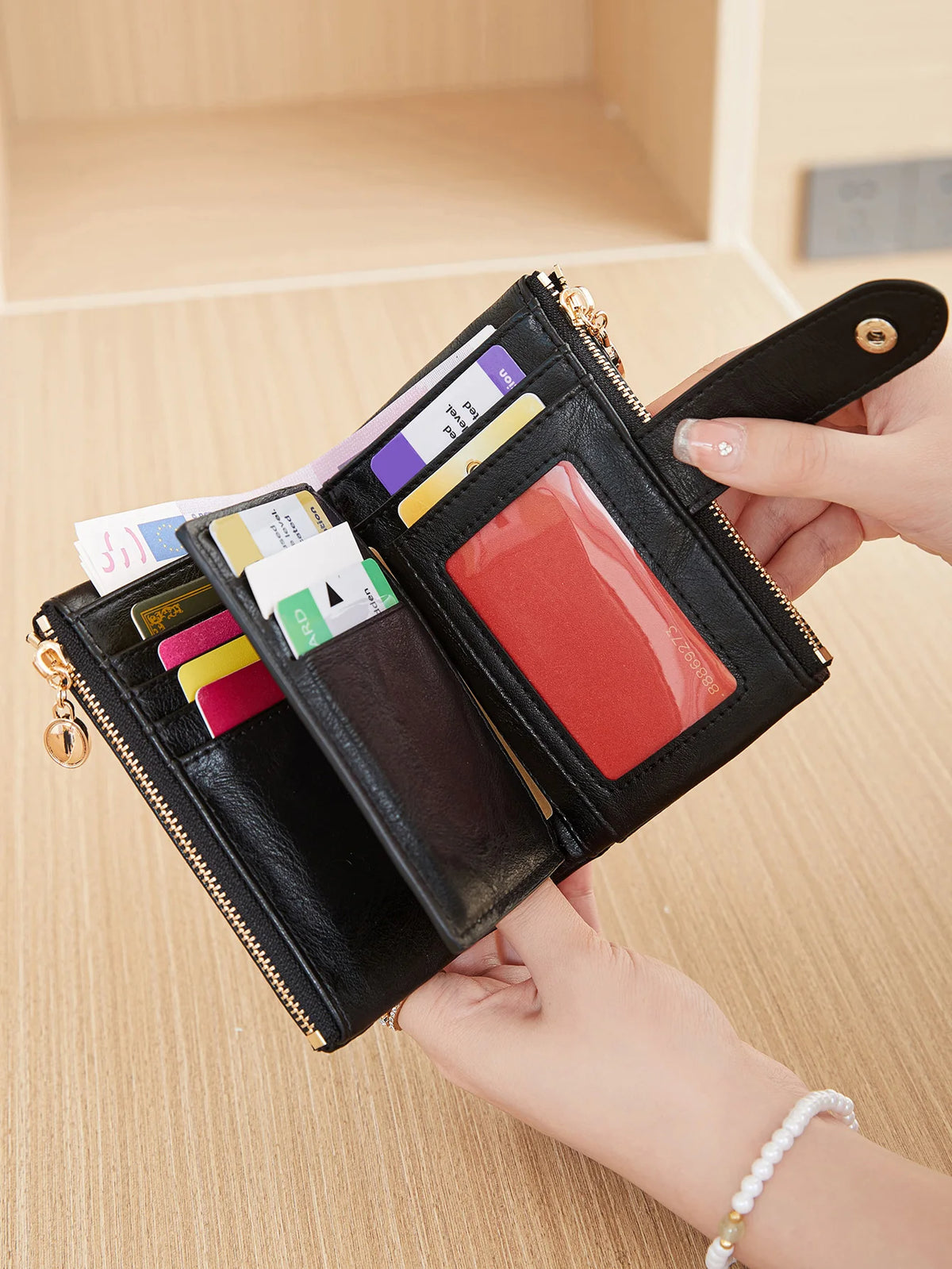 A black leather wallet with gold accents and various cards is held by a hand against a light wooden background.