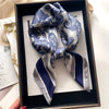 A blue and white paisley silk hair scarf tied in a bow is displayed in a dark wooden frame.