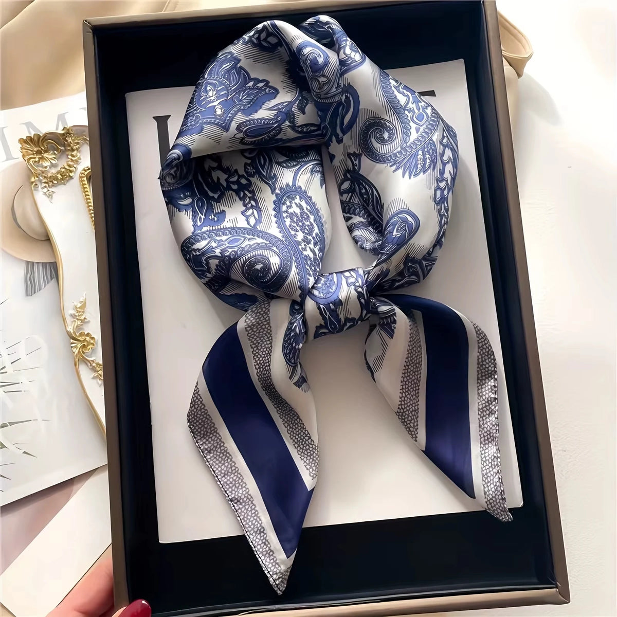 A blue and white paisley silk hair scarf tied in a bow is displayed in a dark wooden frame.