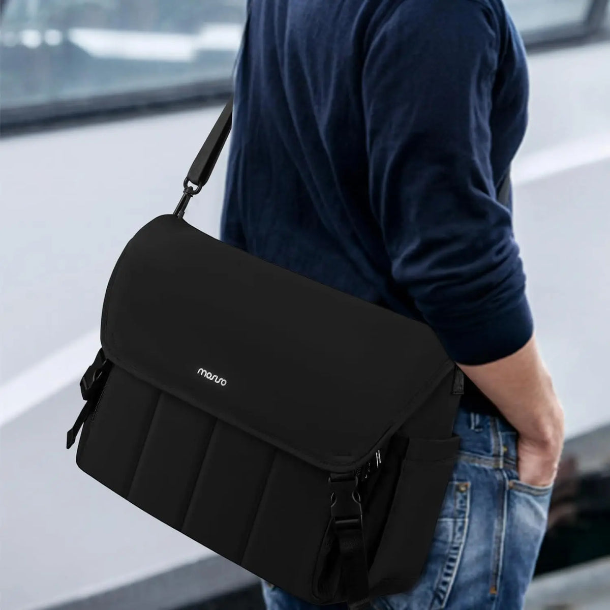 Une housse d'ordinateur portable noire avec une sangle d'épaule est tenue par une personne vêtue d'une chemise bleu foncé et 