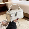 A white quilted woven crossbody bag with a silver chain strap being held by a hand in a bright room.