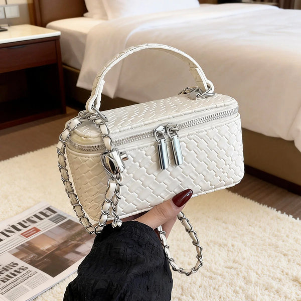 A white quilted woven crossbody bag with a silver chain strap being held by a hand in a bright room.
