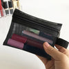 A hand holds a black mesh cosmetic storage pouch filled with various colored makeup items.
