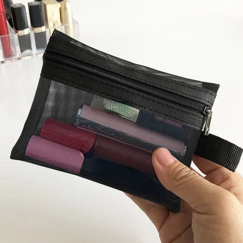 A hand holds a black mesh cosmetic storage pouch filled with various colored makeup items.