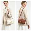 A woman models a beige blazer and white skirt while carrying a brown leather shoulder bag.