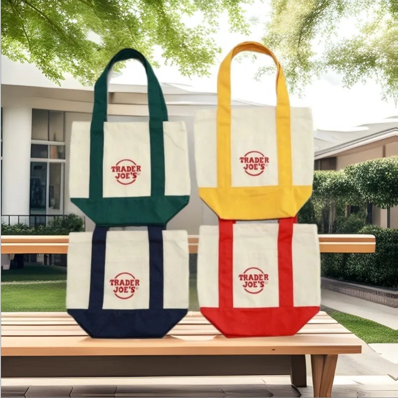 Three canvas bags in green, yellow, and white with red trim displayed on a wooden bench.