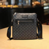 A dark gray men's lightweight crossbody sling bag with a zippered flap resting on a wooden surface.