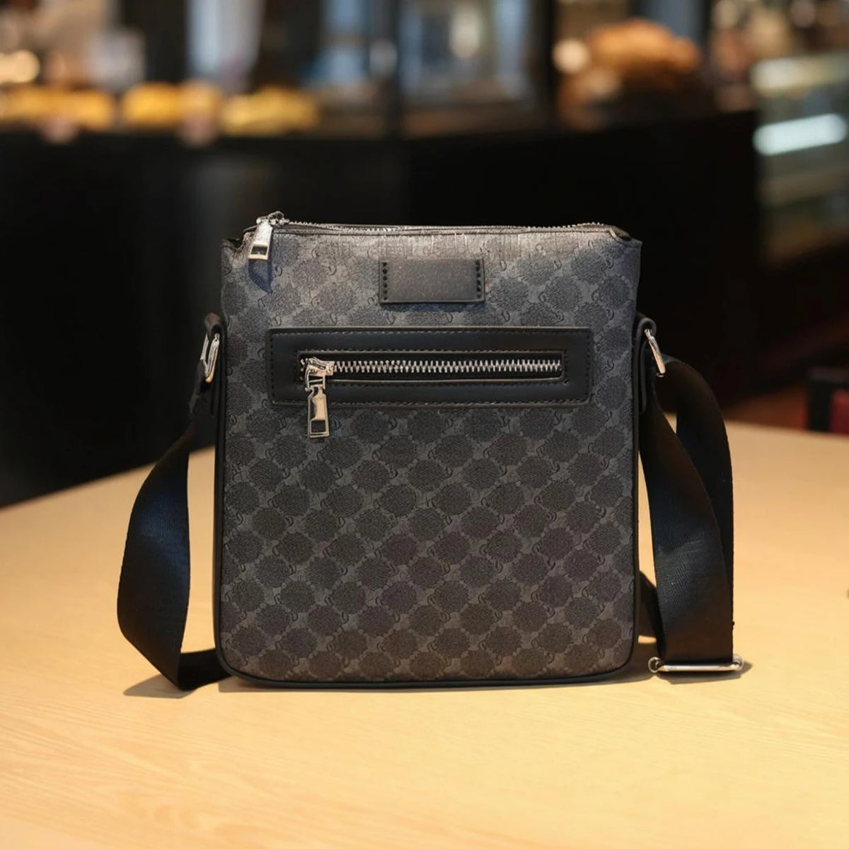 A dark gray men's lightweight crossbody sling bag with a zippered flap resting on a wooden surface.