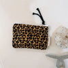 A black leopard print cosmetic bag with a white lining and a black tassel hanging from the top.