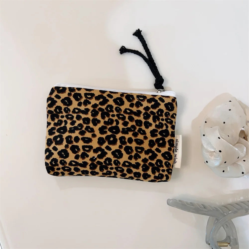 A black leopard print cosmetic bag with a white lining and a black tassel hanging from the top.