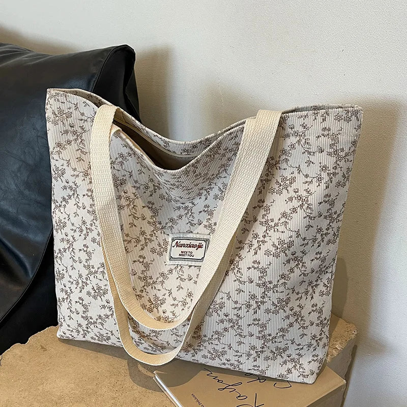 A beige bohemian corduroy tote bag with a subtle floral pattern resting on a light brown box.