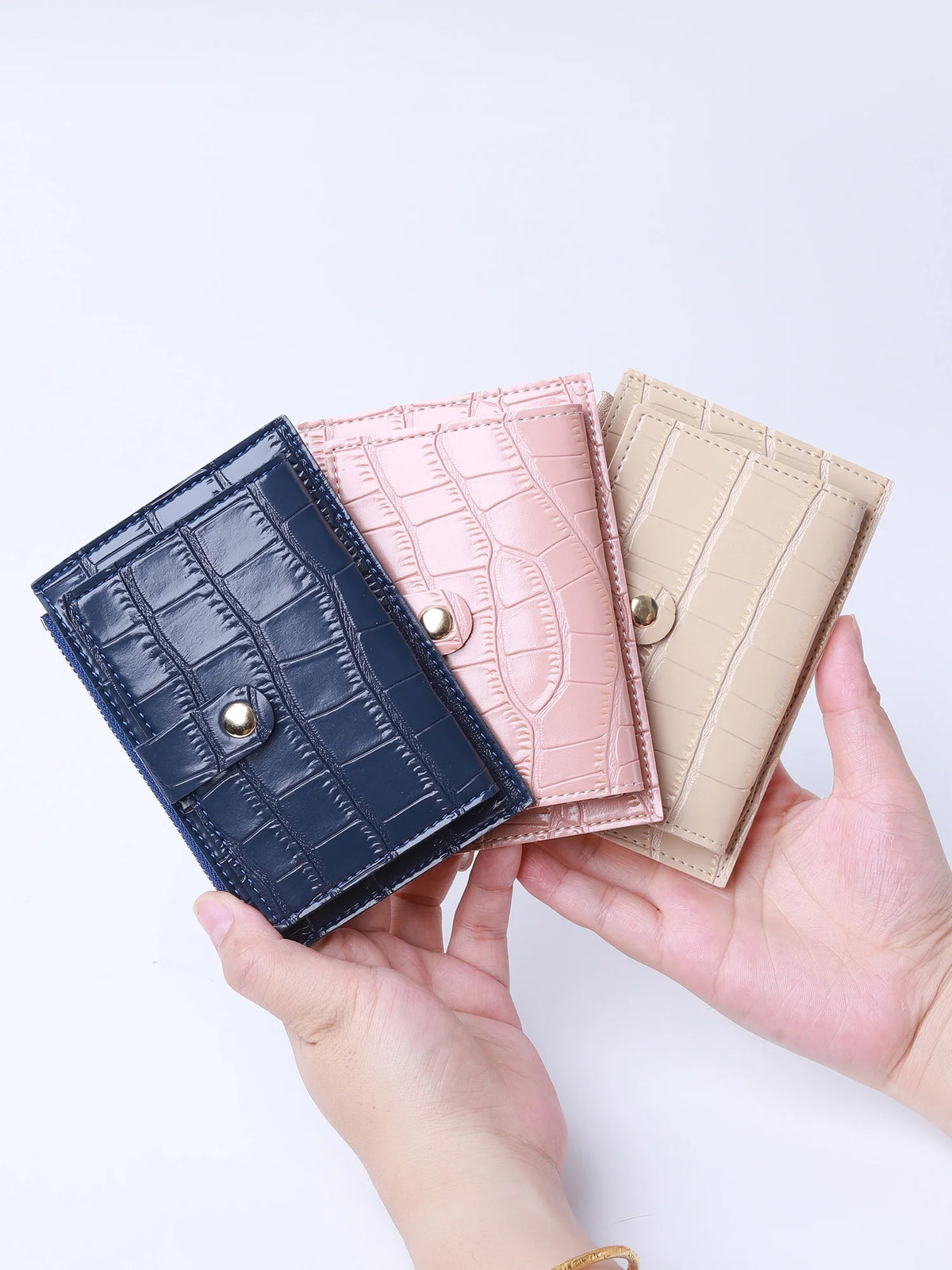 A hand holds a mini crocodile pattern leather card holder in navy blue and blush pink.