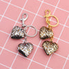 Gold-toned keychain featuring leopard print heart charms on a pink grid background