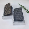 A dark gray geometric print passport wallet displayed in its packaging on a white surface.