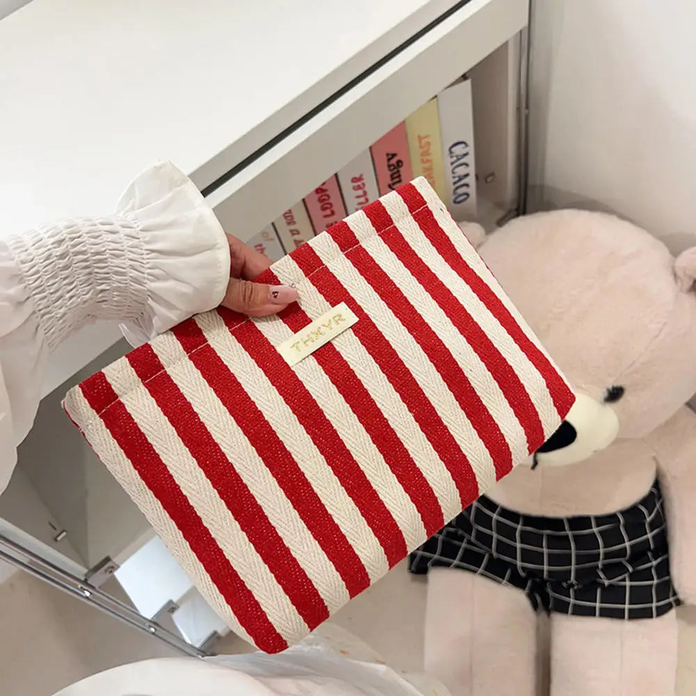 Un bolso de mano tejido a mano a rayas con listones rojos y crema, junto a un gran osito de peluche.