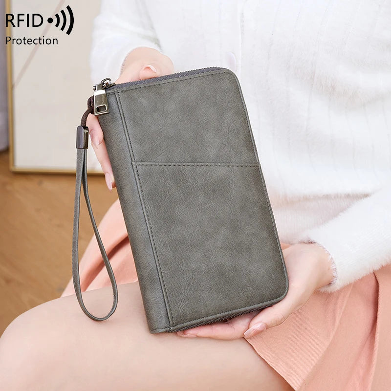 A dark gray leather RFID blocking travel wallet is held by a person in a white top.