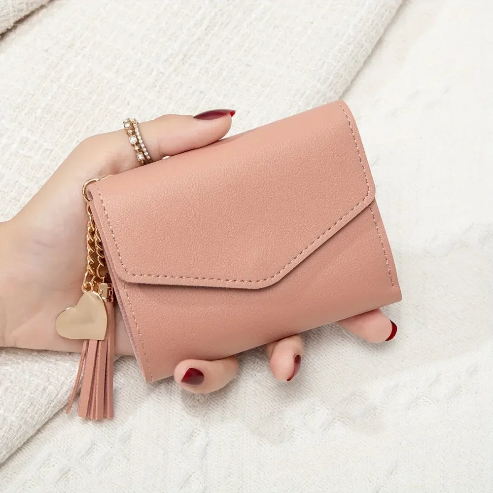 A hand holds a pink PU leather coin clutch wallet with a gold tassel on a white surface.