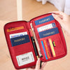 A red travel wallet with slots for passports, credit cards, and other documents is held by a hand.