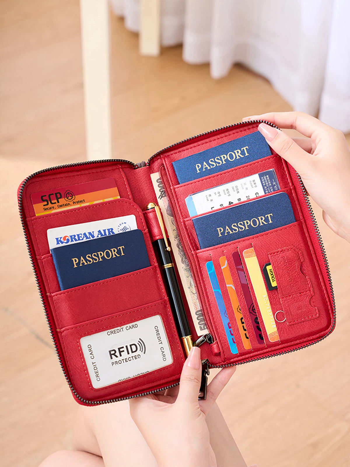 A red travel wallet with slots for passports, credit cards, and other documents is held by a hand.