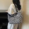 A woman is holding a black and white checkered corduroy tote bag against a light-colored vertical blind.