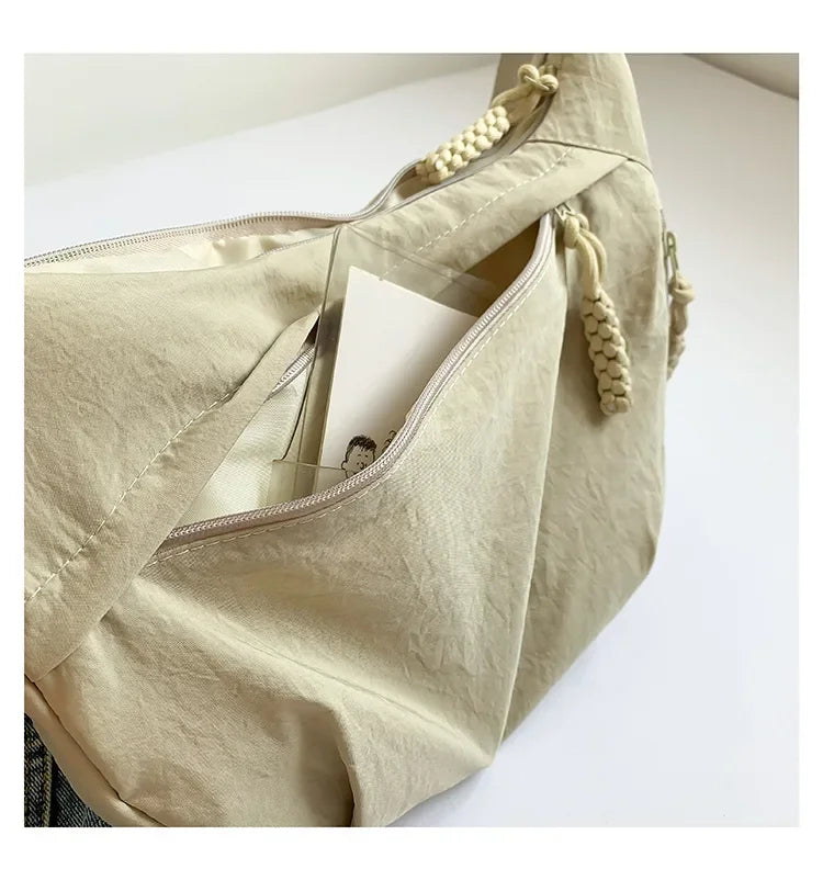 A light beige soft nylon crossbody shoulder bag with a zipper and decorative tassel details.