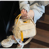 A light beige nylon crossbody bag with a yellow top handle is being held by a person on wooden stairs.
