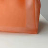 Sac fourre-tout en gelée orange transparente, vue rapprochée sur une surface blanche.