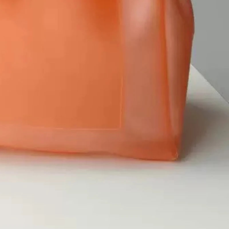 Sac fourre-tout en gelée orange transparente, vue rapprochée sur une surface blanche.