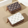 A pair of zippered card holder wallets, one dark brown patterned and one white patterned, resting on a beige surface.