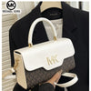 A white Michael Kors letter square crossbody bag with gold hardware is held by a person against a black blazer.
