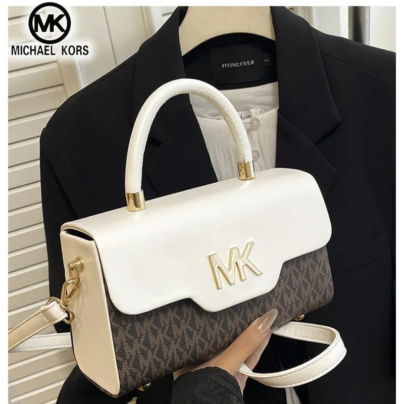 A white Michael Kors letter square crossbody bag with gold hardware is held by a person against a black blazer.