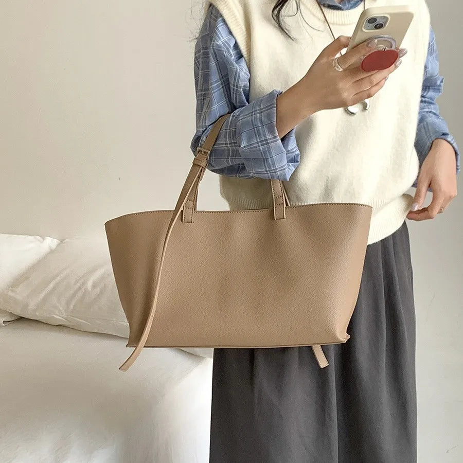 Une femme portant un pull crème et une jupe sombre tient un sac à main en cuir PU beige.