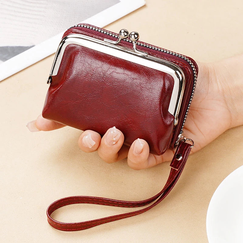 A brown vintage PU leather compact wallet with a silver trim and leather strap is held in a person's hand.