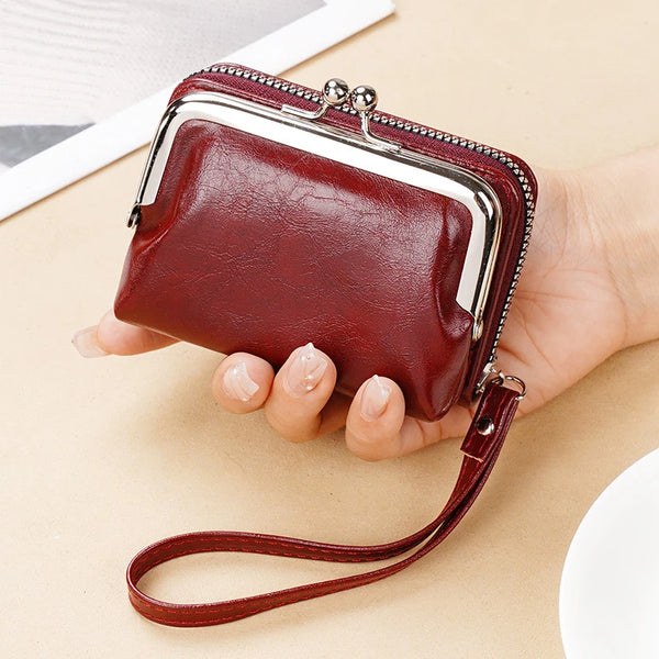 A brown vintage PU leather compact wallet with a silver trim and leather strap is held in a person's hand.
